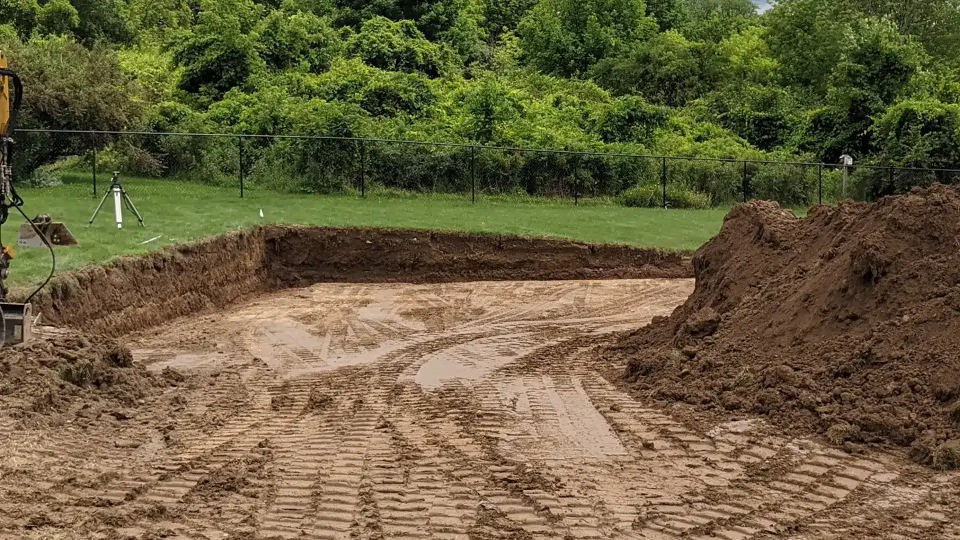 Excavator performing drainage solutions and grading work on a sloped property near Syracuse